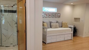 A room with a glass shower enclosure, a white sofa with multiple cushions, and a wall-mounted shelf. - Updated 2 Floor Central Downtown Raleigh Home (Raleigh)
