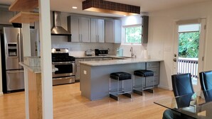 A modern kitchen with stainless steel appliances, grey cabinets, and a glass dining table with blue chairs. - Updated 2 Floor Central Downtown Raleigh Home (Raleigh)