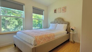 A bedroom with a bed, a window, a bedside table with a vase of flowers, and wall art. - Updated 2 Floor Central Downtown Raleigh Home (Raleigh)