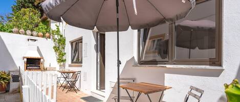 A patio with a table, chairs, a grill, and an umbrella.