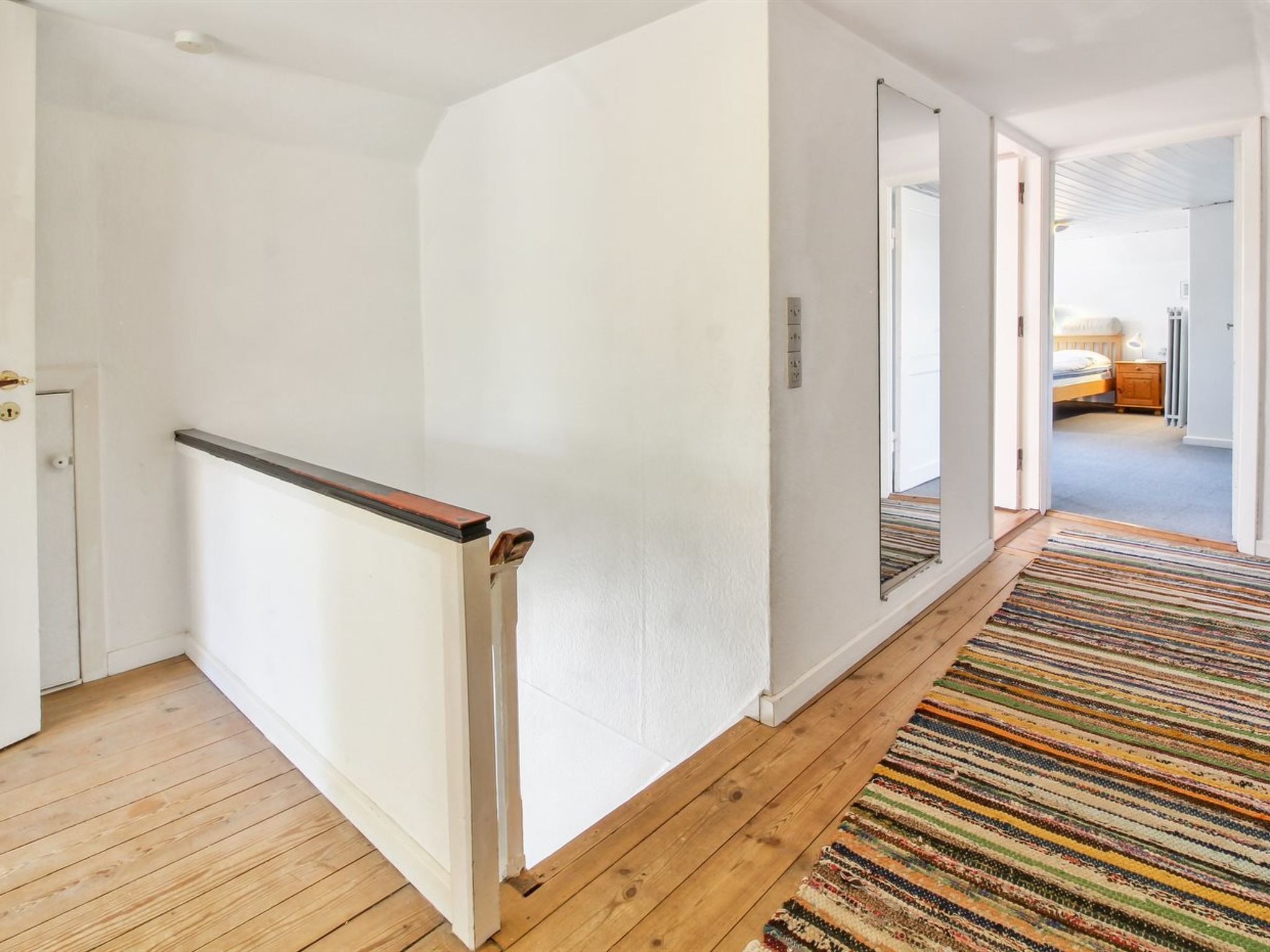 Un couloir doté d’un plancher en bois, de murs blancs et d’un tapis à rayures.