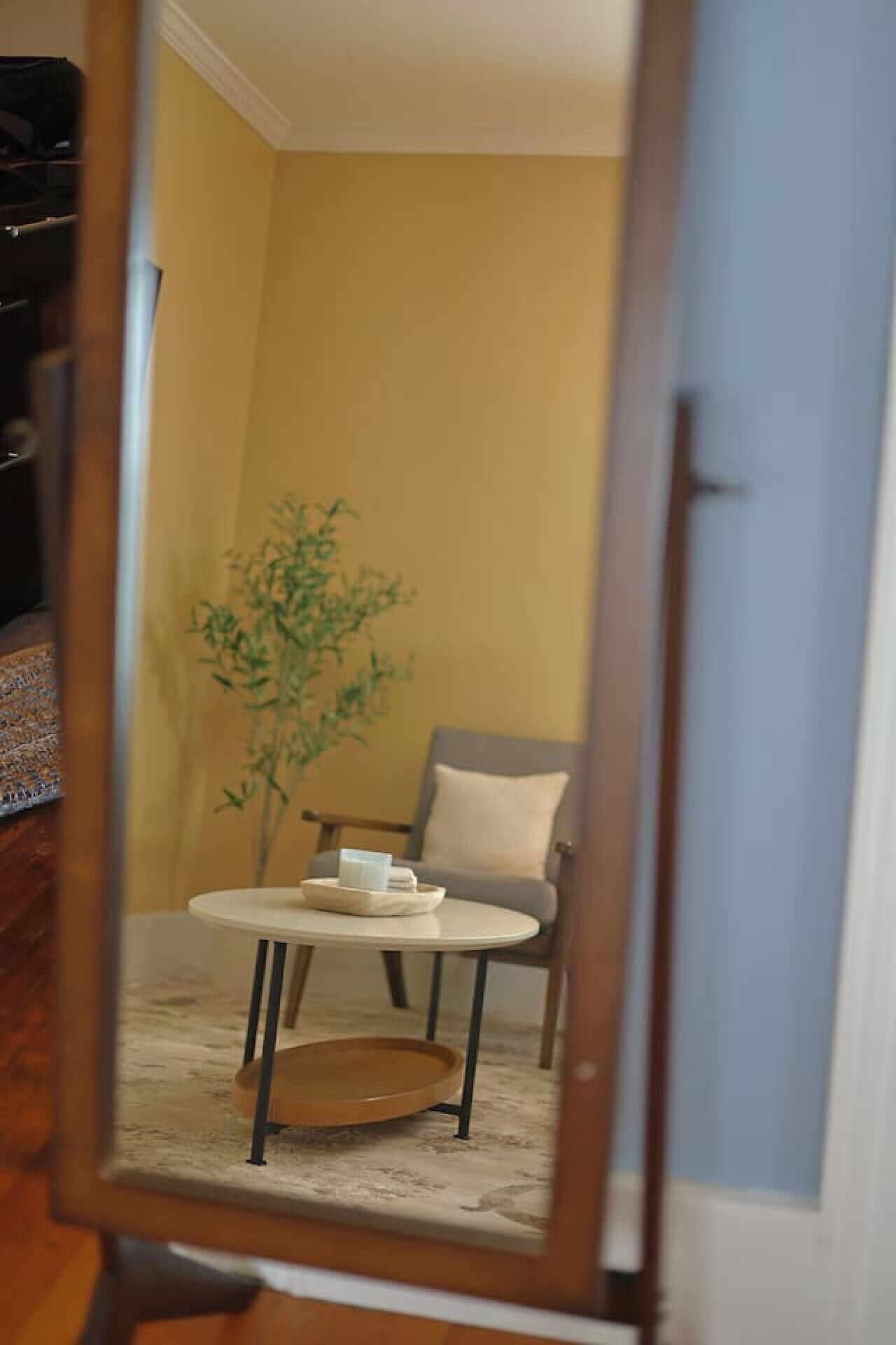 A room with a yellow wall, a gray armchair, a small round table, and a potted plant.