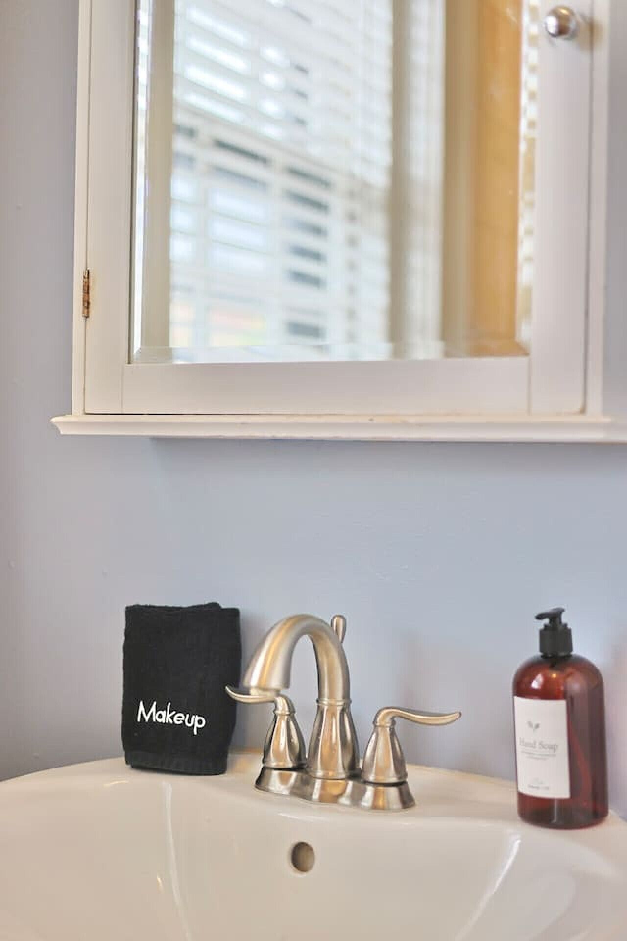 A bathroom sink with a silver faucet, a black makeup bag, and a bottle of hand soap.