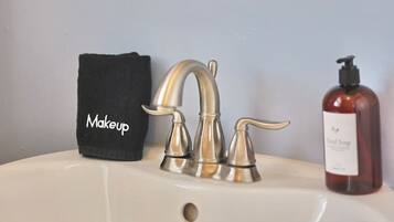 A bathroom sink with a silver faucet, a black makeup bag, and a bottle of hand soap.