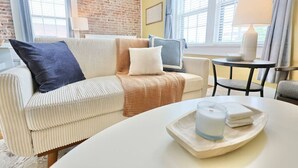Una habitación acogedora con un sofá blanco, una mesita redonda con un candelabro, y una pared de ladrillo.