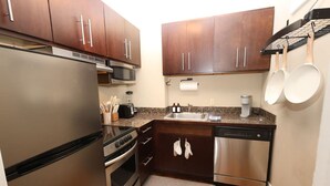 Cocina compacta con electrodomésticos de acero inoxidable, armarios de madera oscura y encimera de granito.