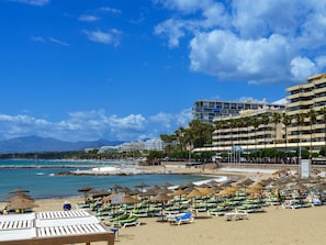 A beach with sun loungers and umbrellas, a hotel in the background, and a clear blue sky. - Alvarito Playa by Interhome (Marbella)