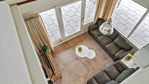 Ein modernes Wohnzimmer mit einem Ecksofa, zwei kleinen weißen Tischen und einem großen Fenster mit Vorhängen.