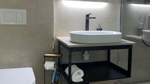 Ein modernes Badezimmer mit Toilette in Weiß, einem runden Waschbecken mit schwarzer Ablagefläche und einem Spiegel darüber.