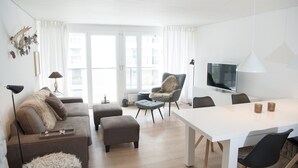 Ein modernes Wohnzimmer mit einer Couch, einem Hocker und einem Esstisch mit Stühlen.
