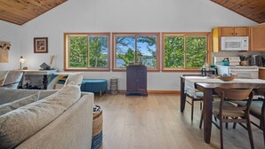 A cozy interior with a wooden ceiling, a dining area, a kitchen with a microwave, and large windows overlooking greenery.
