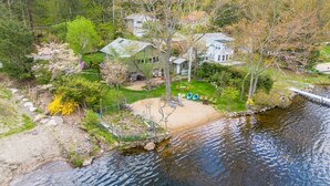 A lakeside property with a house, a dock, and a sandy area for outdoor activities.