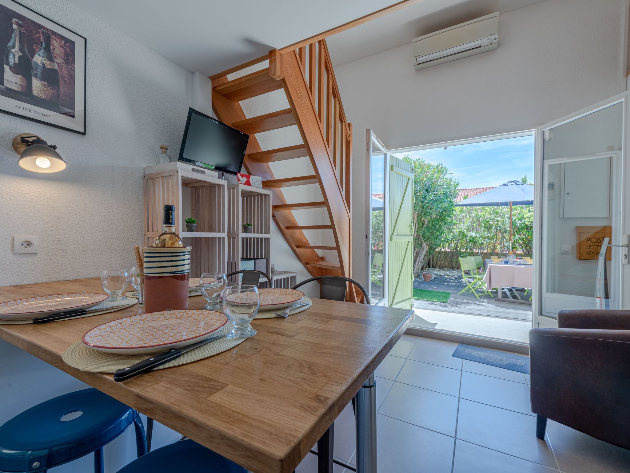 A modern kitchen with a wooden staircase, a dining table set with plates and glasses, and a television on the wall.