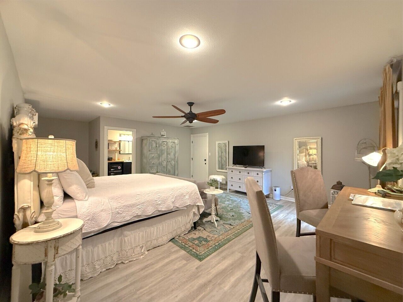 A bedroom with a bed, bedside tables, a desk, a chair, a television, a ceiling fan, and a dresser.