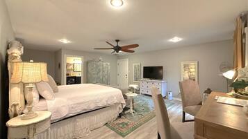 A bedroom with a bed, bedside tables, a desk, a chair, a television, a ceiling fan, and a dresser.