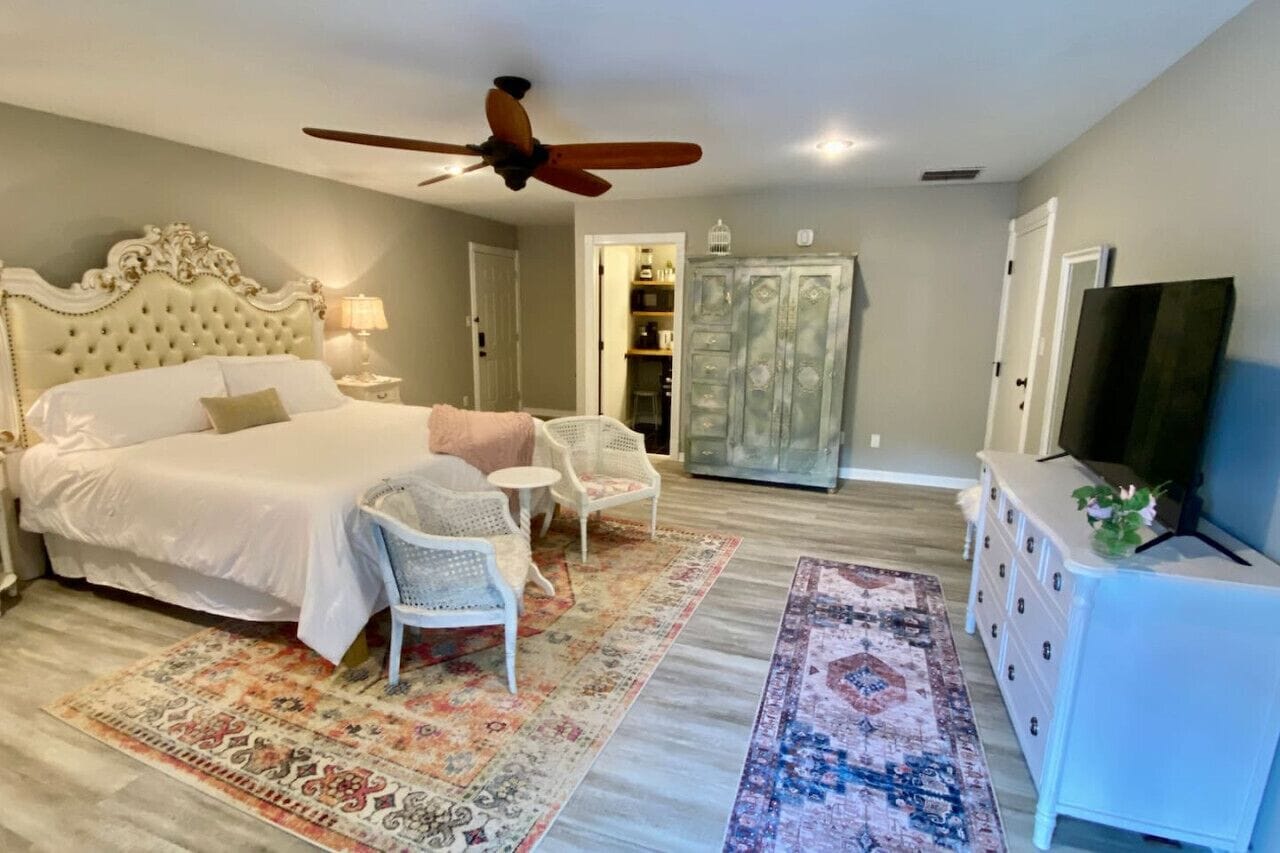 A bedroom with a large bed, a ceiling fan, a television, a wardrobe, and a small table with chairs.