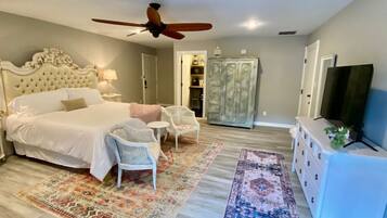 A bedroom with a large bed, a ceiling fan, a television, a wardrobe, and a small table with chairs.