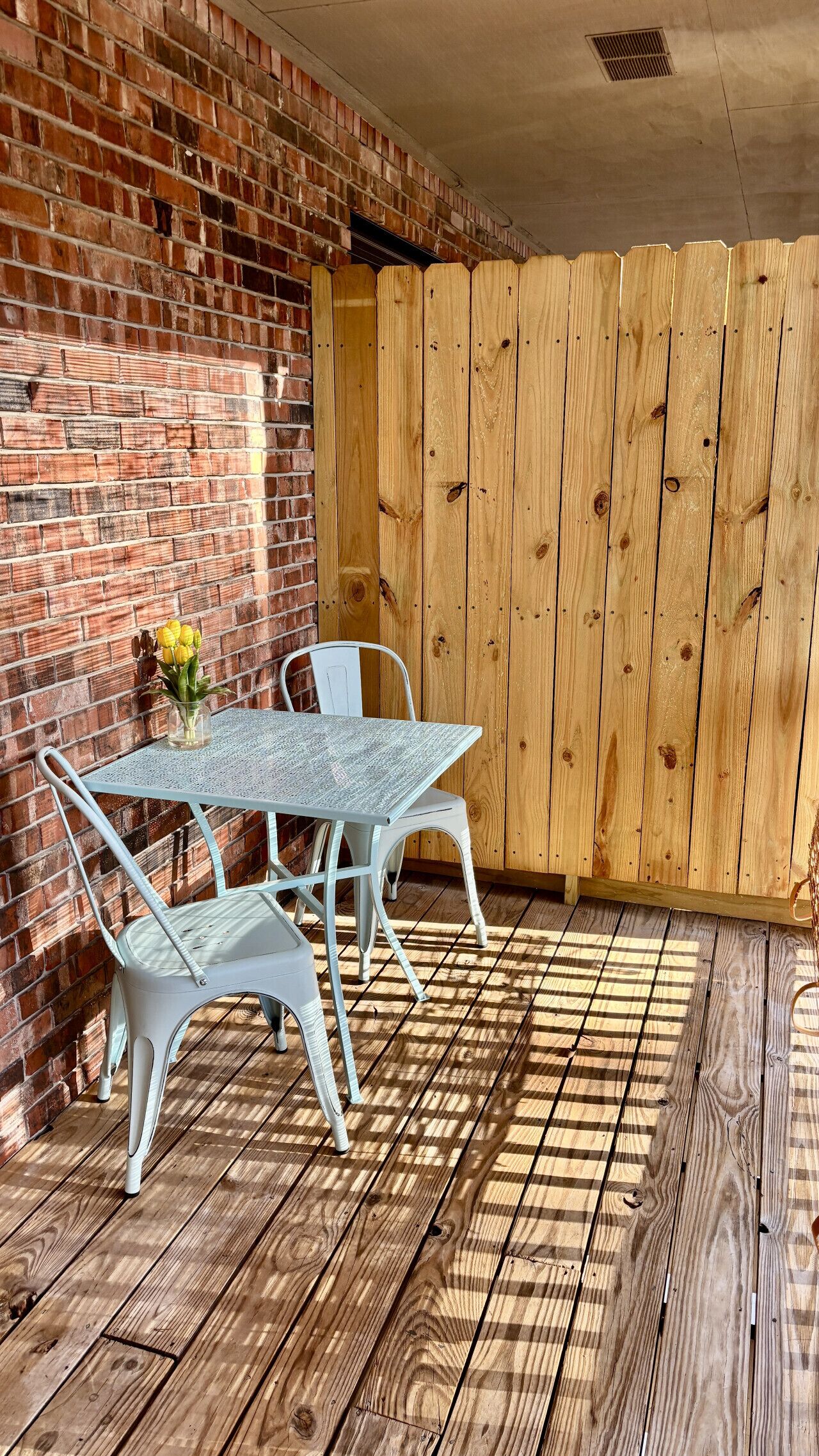 A patio area with a brick wall, a wooden fence, and a table with chairs.