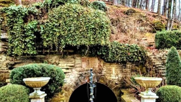 A stone archway with a circular opening, flanked by two stone urns, and surrounded by lush greenery and a stone wall. - Downtown+FreePark+Wifi Main St. Ste 201 (Eureka Springs)