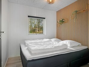 Relax in a serene bedroom with a neatly made bed, a window overlooking trees, and a wooden slat wall.