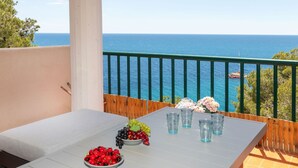 A balcony with a table set for two, featuring a bowl of cherries and grapes, and a vase of flowers.