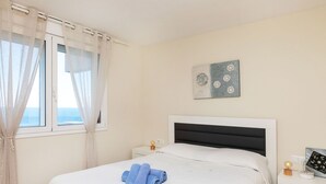 A hotel room with a bed, a bedside table, a nightstand, a window with curtains, and a wall-mounted artwork.