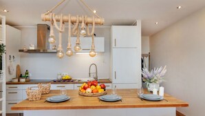 A modern kitchen with a central island, wooden stools, and a hanging light fixture.