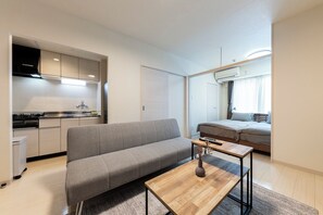 A modern apartment with a grey sofa, a wooden coffee table, a kitchen with a stove, and a bed with a window. - HILLS SAPPORO 201 (Sapporo)
