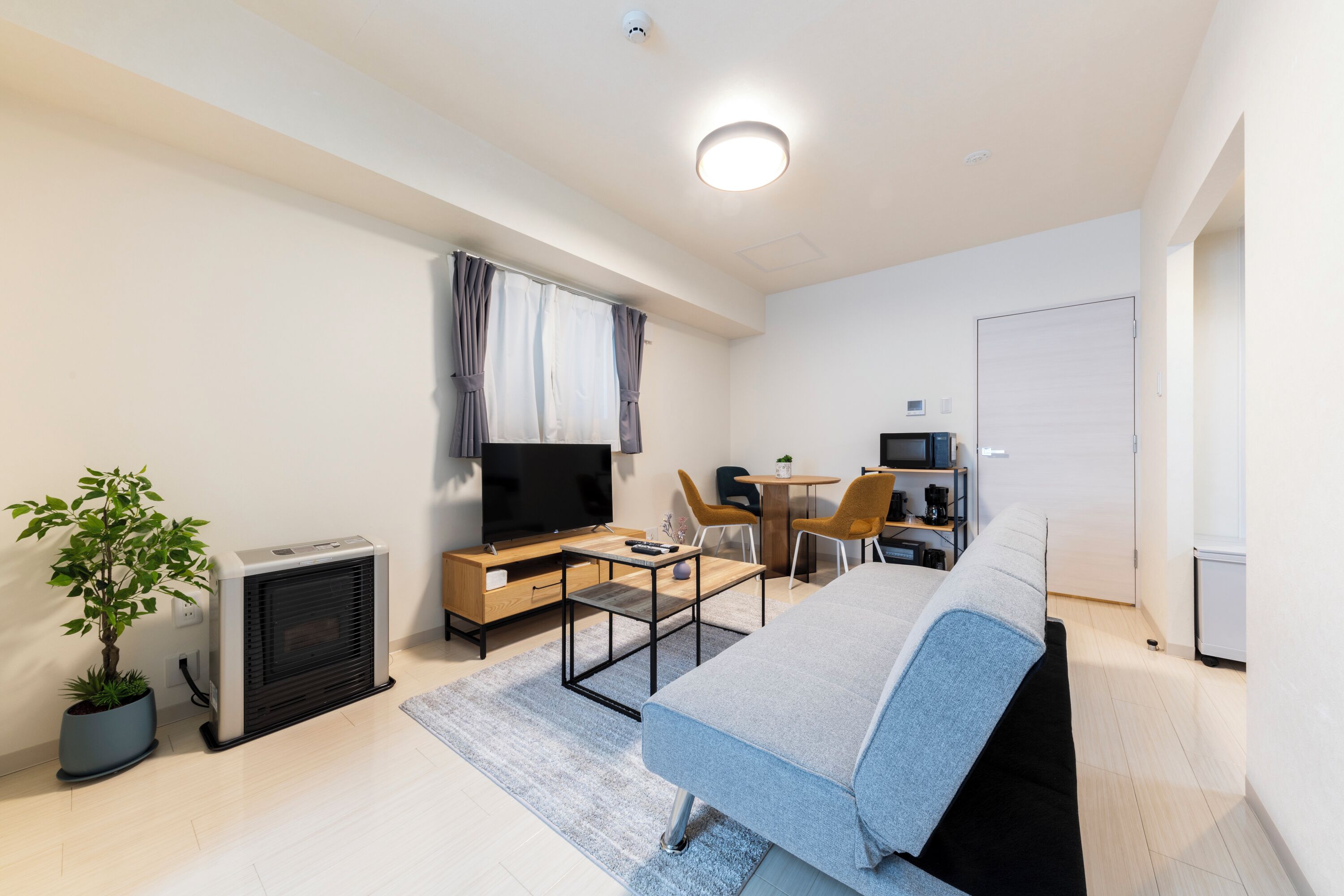 Habitación de hotel moderna con cama, escritorio, silla, televisor, mesita pequeña y planta en maceta.