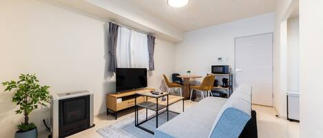 Habitación de hotel moderna con cama, escritorio, silla, televisor, mesita pequeña y planta en maceta.