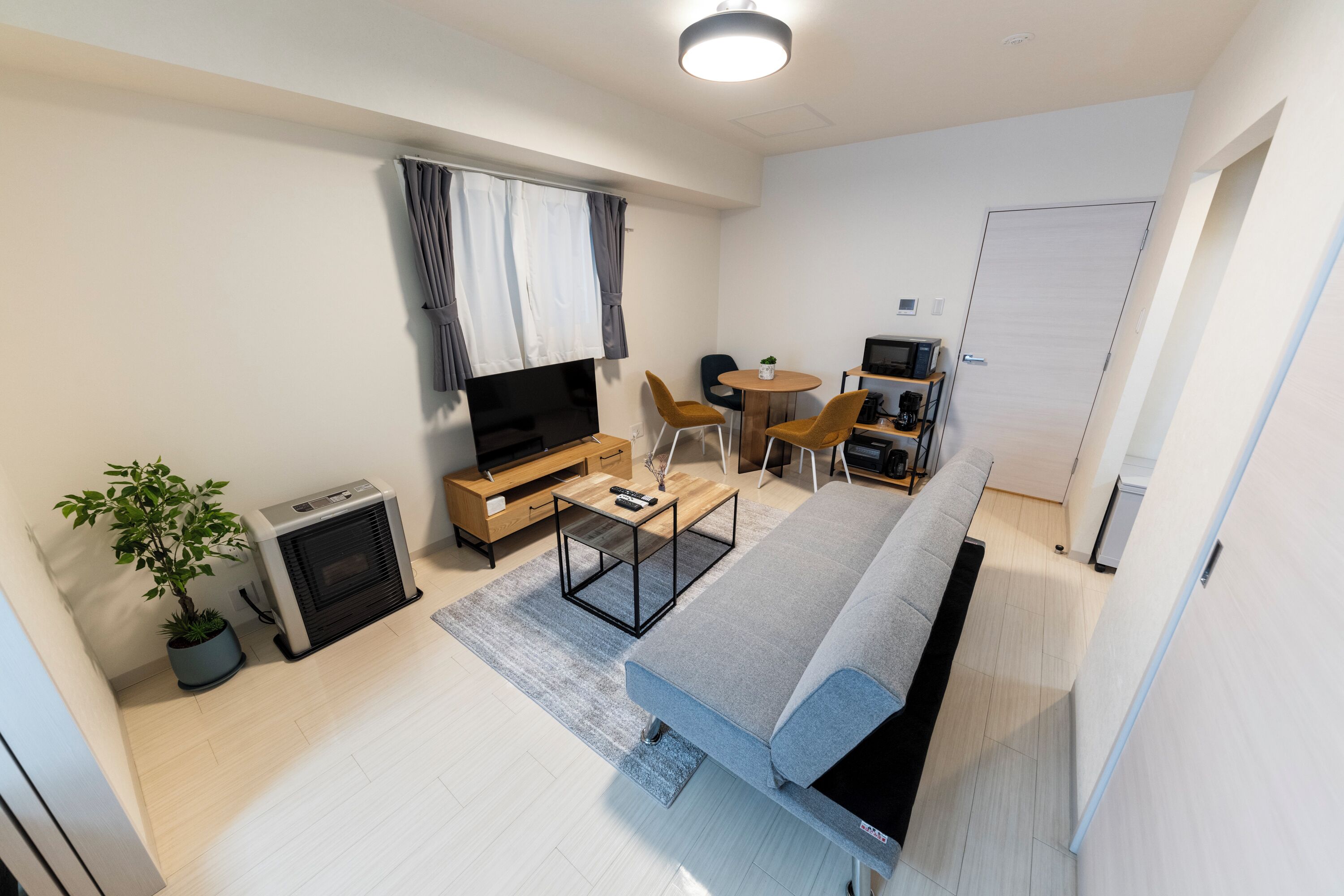 A modern living room with a sofa, TV, and a small dining area with chairs and a table.