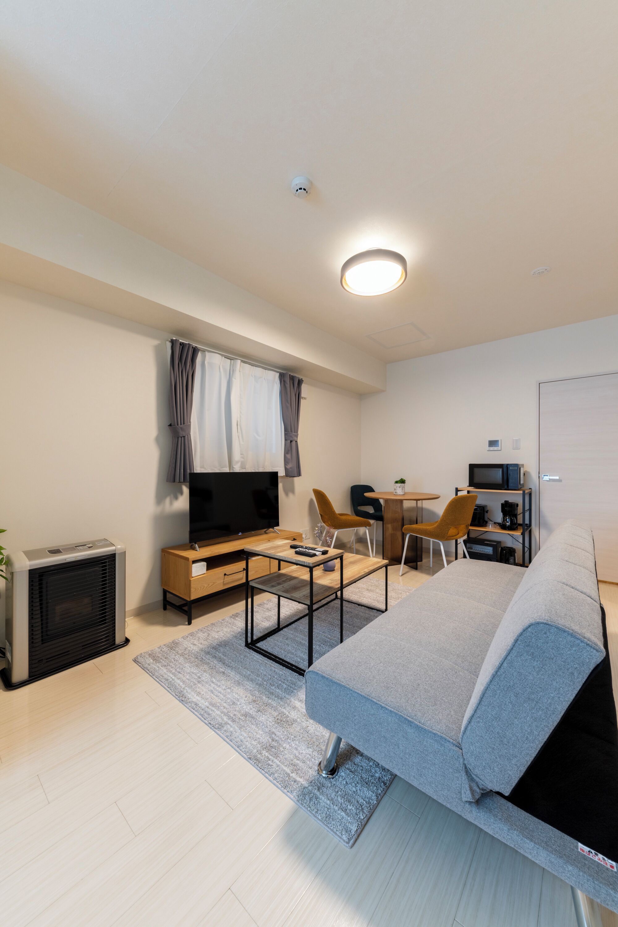 A modern hotel room with a bed, a TV, a desk with a chair, a small table, and a microwave.