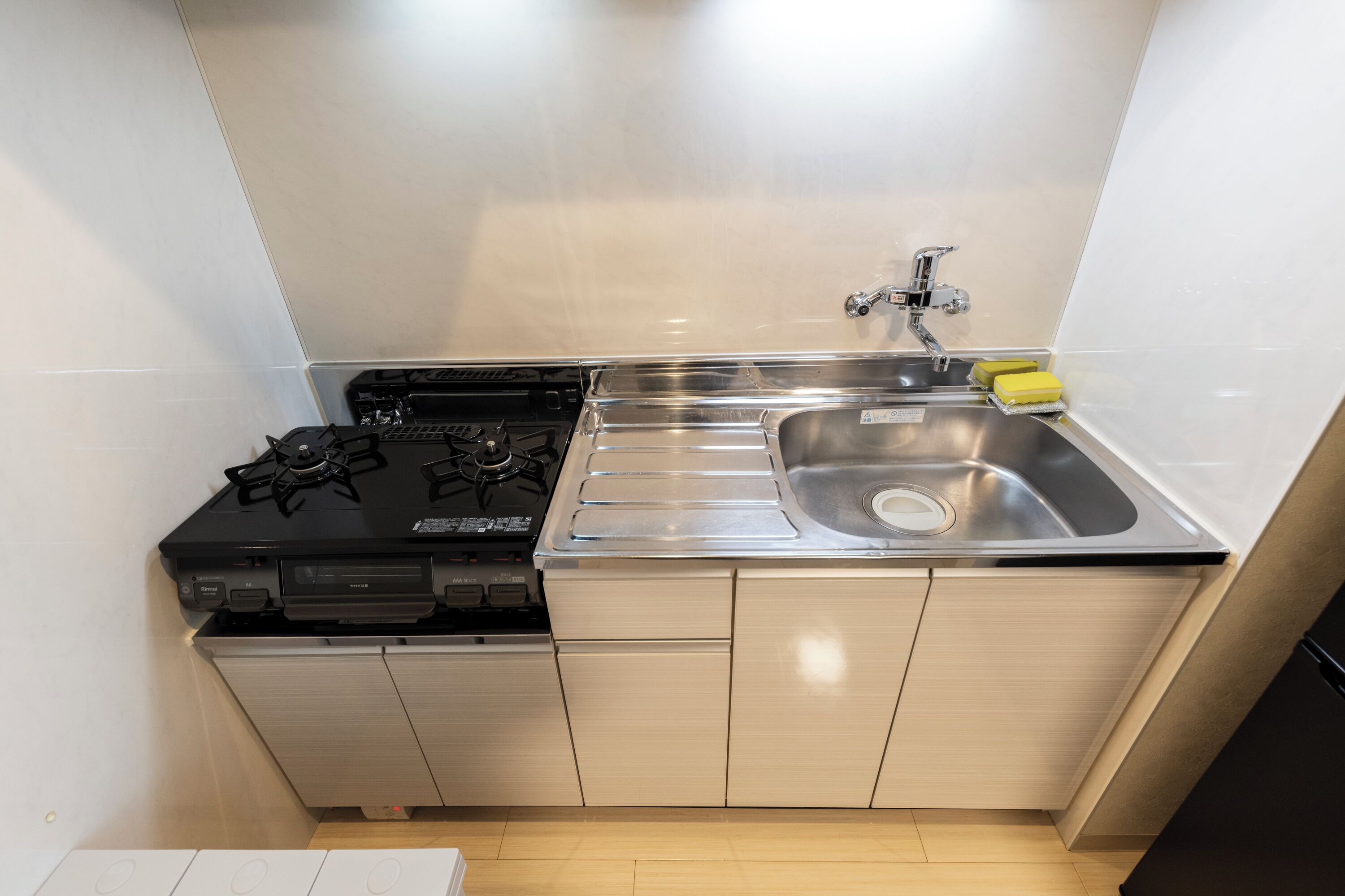 Una cocina compacta con estufa a gas, pileta de acero inoxidable y alacenas de madera.