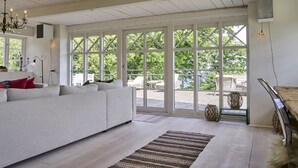 Amplia sala de estar con un sofá blanco, un tapete estampado y grandes ventanales con vistas al exterior.