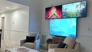 A modern living room with a ceiling fan, a flat-screen TV mounted on the wall, and two beige armchairs. - Freshly renovated condo in the heart of College Station! Sleeps 6 (College Station)