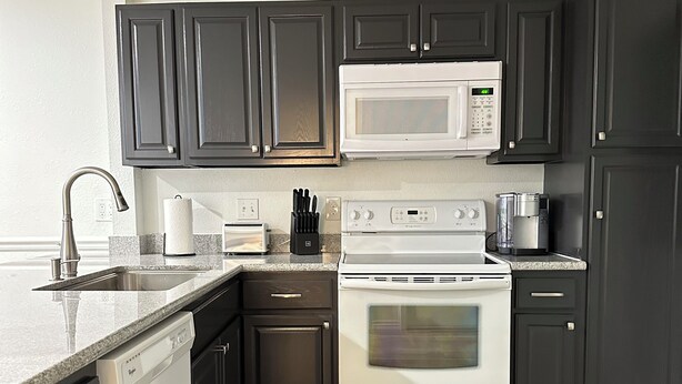 A modern kitchen with dark cabinets, a white microwave, a built-in oven, and a dishwasher. - Freshly renovated condo in the heart of College Station! Sleeps 6 (College Station)
