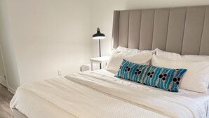 A neatly made bed with white bedding and a patterned pillow, a bedside table with a lamp, and a wooden floor. - Freshly renovated condo in the heart of College Station! Sleeps 6 (College Station)