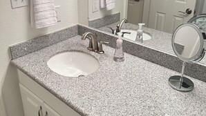 A bathroom with a granite countertop, a white sink, a mirror, and two towels hanging on hooks. - Freshly renovated condo in the heart of College Station! Sleeps 6 (College Station)