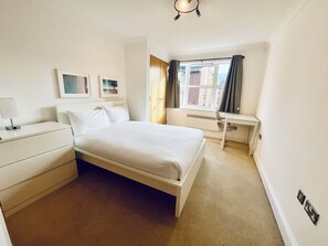 Cozy retreat with a neatly made bed, bedside table, and desk, offering a peaceful space to unwind.