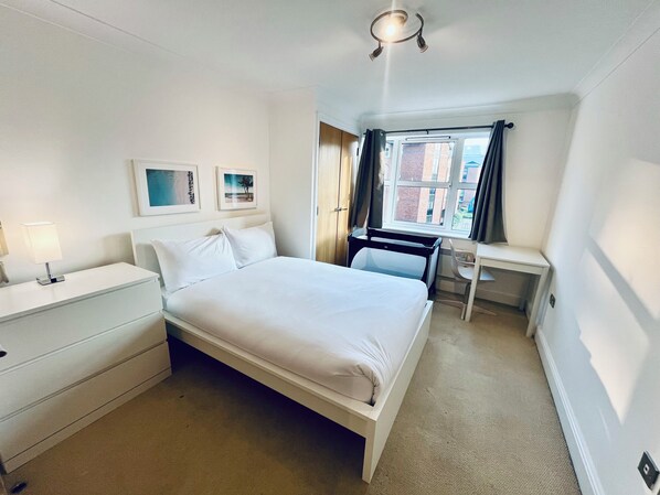 Comfortable room with a neatly made bed, bedside table, and desk with chair.