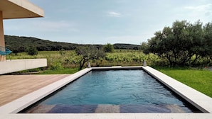 Una piscina rectangular con muelle de madera y borde de hormigón, rodeada de exuberante vegetación y viñedos.