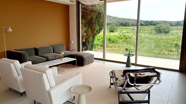 Una sala de estar moderna con un sofá, sillas, una mesa de centro y vistas a un paisaje exuberante a través de grandes ventanales.