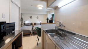 A compact kitchen with a sink, a countertop, and a chair. There is a bed with two pillows and a bedside table with a lamp. - HILLS SAPPORO 203 (Sapporo)