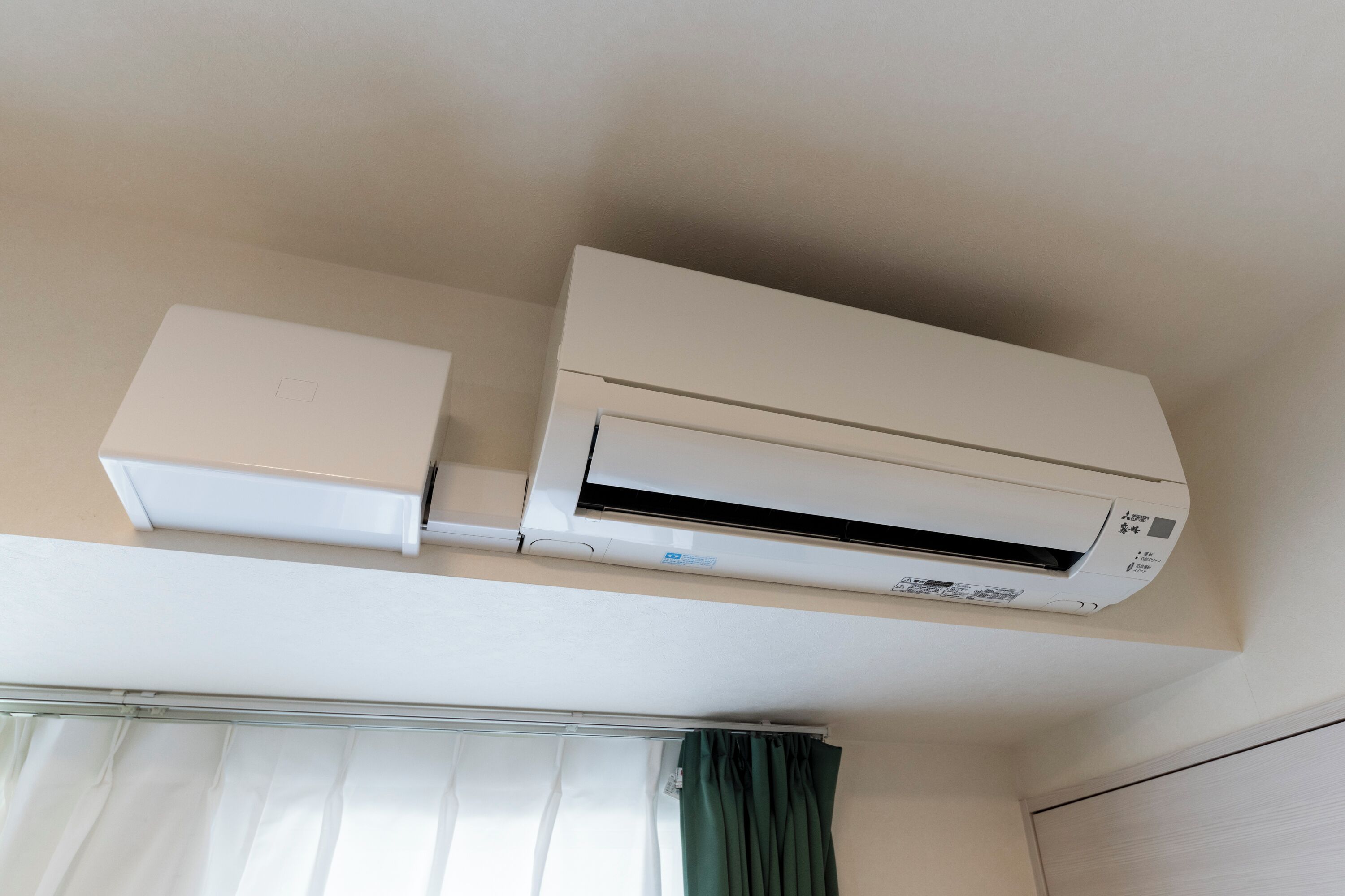 A ceiling-mounted air conditioning unit in a room with a window and curtains.