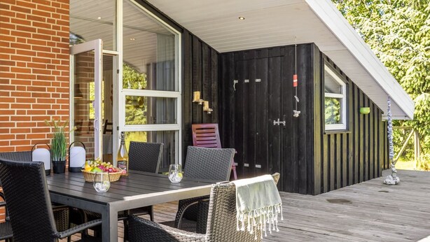 An outdoor dining area with a table and chairs, a brick wall, and a wooden deck. - "Olli" - 600m from the sea by Interhome (Jerup)