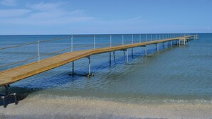 Eine Holzstege, der sich in ruhiges Wasser erstreckt, mit blauem Himmel.