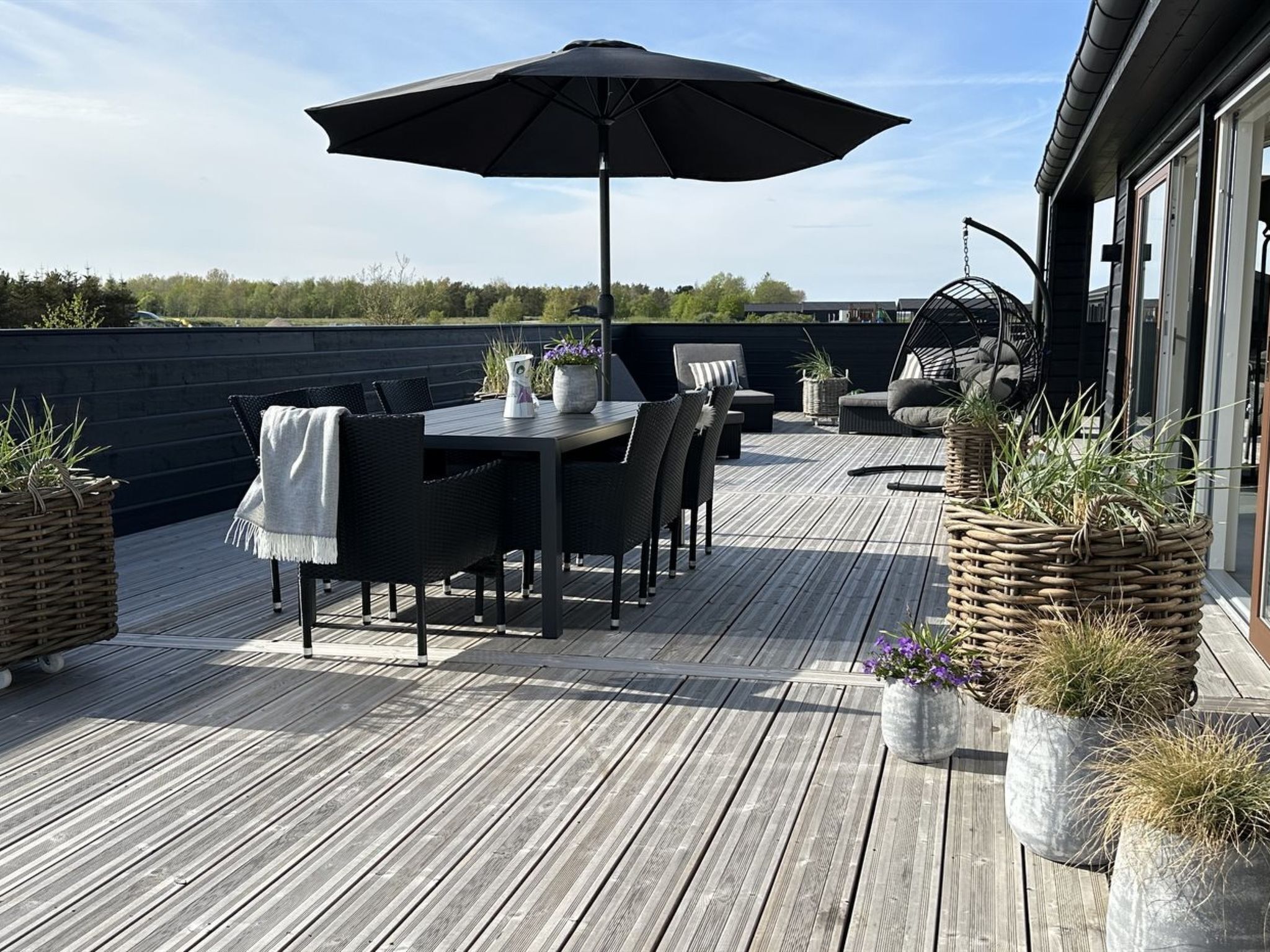 Een houten terras met een tafel, stoelen, een hangstoel en potplanten.