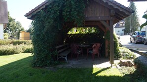 Ein hölzerner Pavillon mit Tisch und Stühlen, umgeben von einem gepflegten Rasen und viel Grün.