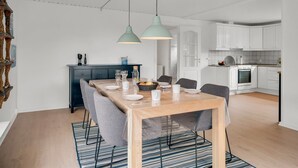 Una cocina moderna con armarios blancos, horno empotrado y comedor con mesa y sillas de madera.