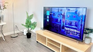 A flat-screen TV on a wooden stand in a room with a wooden floor, a potted plant, and a floor lamp. - Bungalow | Upper Level | CT Train | Spruce Meadow (Calgary)